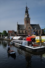 A cargo of cheese being transported down a canal next to a cheese market taking place in front of