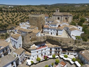 Spanish village with historic buildings, church and olive groves under a sunny sky, surrounded by a