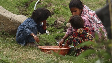 A woman and two children crouching near a wash basin in a rural area, engaged in washing