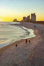 People walking and playing on the beach as the sun sets over the Gulf of Mexico at Gulf Shores,