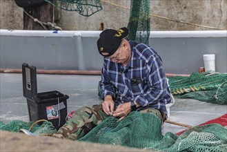 Commercial fisherman on his shrimp boat repairing his nets at the Biloxi Small Craft Harbor in