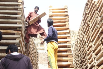 Workers handling lumber, standing between stacks of wooden planks in a construction area, Jammu and