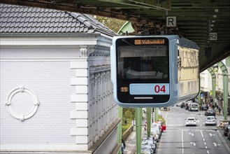 A suspension railway runs above a busy city street with cars and buildings in Wuppertal Vohwinkel