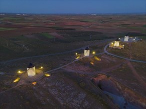Night shot of several illuminated windmills on hills in a wide field landscape at dusk, aerial
