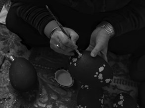Close-up of hands meticulously painting decorative patterns on eggs, showcasing traditional