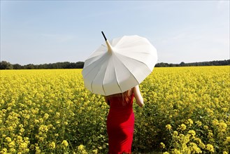 Woman standing in a rape field with a white parasol