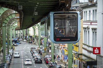 A suspension railway runs above a busy city street with cars and buildings in Wuppertal Vohwinkel