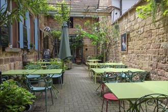 A cosy outdoor area of a cafe with green tables and chairs, surrounded by plants and brick walls,