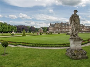 Large, well-kept garden with a detailed stone figure and a castle in the background, old red brick