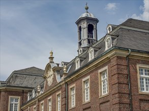 A part of a historic castle with a clock tower and many windows under a partly cloudy sky, old red