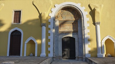 Ottoman Library, Yellow historical facade of a building with an ornate entrance arch, inscriptions