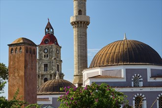 Suleiman Mosque, minaret and domes next to bell tower with red bricks, surrounded by flowers and