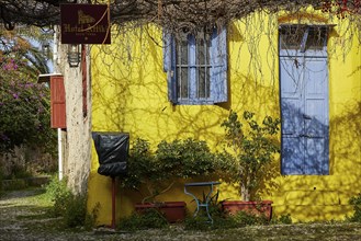 A yellow house with blue windows, surrounded by flowers and shadows, Rhodes Old Town, Rhodes Town,