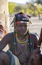 Hakaona woman with traditional kapapo hairstyle and colourful necklaces, in the morning light,