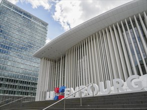 Modern building in Luxembourg with glass facade and striking columns next to a skyscraper, under a