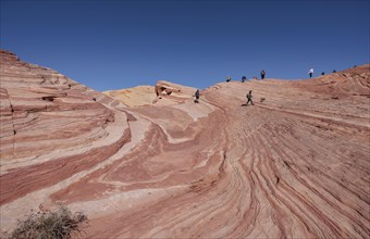 Park visitors on the layered sandstone rock formations in the Fire Wave area of Valley of Fire