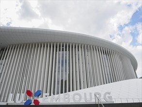 Large modern building in Luxembourg with glass facade and vertical columns under a slightly cloudy