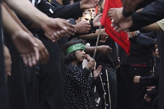 Child holding a red flag among people dressed in black, participating in a solemn procession, Jammu