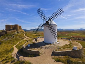 White painted windmill on a hill with a castle in the background and fields under a blue sky,