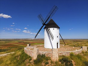 A single windmill on a hill under a bright blue sky in a vast summer landscape, aerial view,