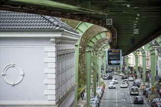 A suspension railway runs above a busy city street with cars and buildings in Wuppertal Vohwinkel