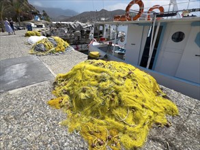 Yellow fishing net lying on quay in front of fishing boat in small harbour of Agia Galini, Agia