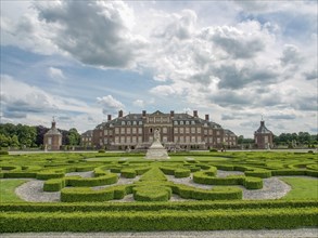 Large historic castle with manicured hedges forming a labyrinth under a cloudy sky, old red brick