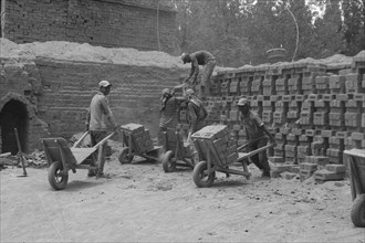 Group of men working together with wheelbarrows and bricks in a construction site outdoors, Jammu