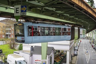 A suspension railway runs above a busy city street with cars and buildings in Wuppertal Vohwinkel