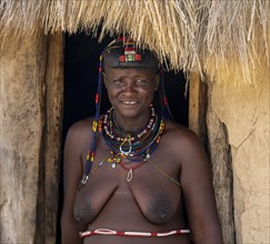 Hakaona woman with traditional kapapo hairstyle, in the entrance of her mud hut, portrait, in the