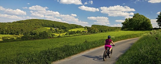 Cyclist in hilly landscape with blue sky and clouds, Wetter (Ruhr), Ruhr area, North