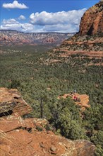 Hikers climb to the top of a red rock sandstone formation along the Devil's Bridge Trail in Sedona,