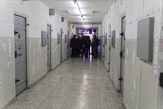 Group of people in the corridor of a prison with grey doors and neon lighting,