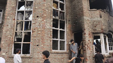 People gather around a multi-story damaged brick building with several broken windows, Encounter,