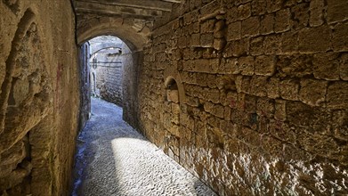 A narrow alleyway with stone walls, flooded with light and shadow, Old Town of Rhodes, Rhodes Town,