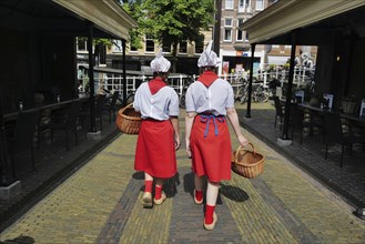 Two Dutch cheese girls in traditional tracht and carrying baskets of cheese, wander through the