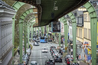 A suspension railway runs above a busy city street with cars and buildings in Wuppertal Vohwinkel