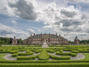 Historic castle with decorative hedges and extensive garden under a slightly cloudy sky, old red