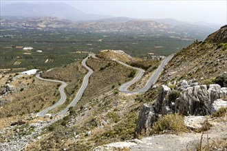Mountain road with serpentines above south of in the background fertile green Messara plain with