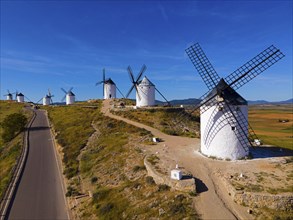 Series of windmills along a road on a sunny hill in a wide summer landscape, aerial view,