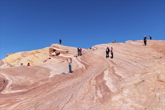 Hikers on layered sandstone rock formations in the Fire Wave area of Valley of Fire State Park near