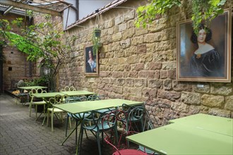 A picturesque garden area of a cafe with green tables and chairs, decorated with portraits on the