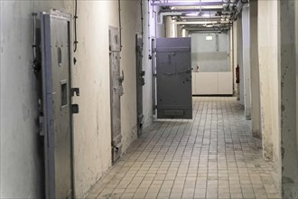 Corridor in a prison with metal cell doors and tiled floor. Gloomy and deserted atmosphere,
