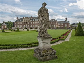 Impressive stone figure in front of a large castle, surrounded by a well-kept garden and colourful