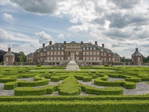 Historic castle with decorative hedges and manicured garden under a cloudy sky, old red brick