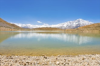 A pristine alpine lake reflects the surrounding Himalayan mountains. The lake is a pilgrimage point