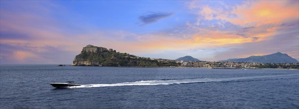 Italy, scenic sunset over Procida Island near Naples with boat approaching it from afar, Europe