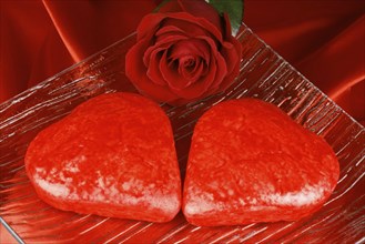 Two red heart shaped cakes and a rose over a red background for Valentine's Day