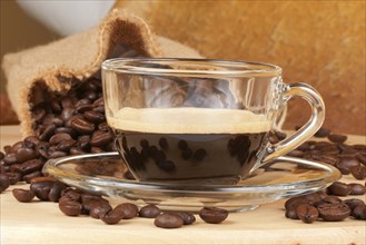 Close-up of a glass cup with italian espresso over a wooden table, surrounded by coffee beans