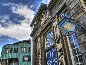 Historic building with ornate Tor tor and blue lantern next to a modern extension under a blue sky,